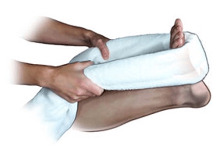 Mãos enrolando uma toalha em volta da planta do pe para puxar os dedos em direção ao corpo, demonstrando um alongamento da fáscia plantar e da panturrilha.
