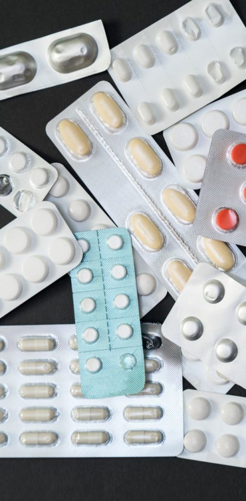 Diversas cartelas de comprimidos e cápsulas de cores variadas espalhadas sobre fundo escuro