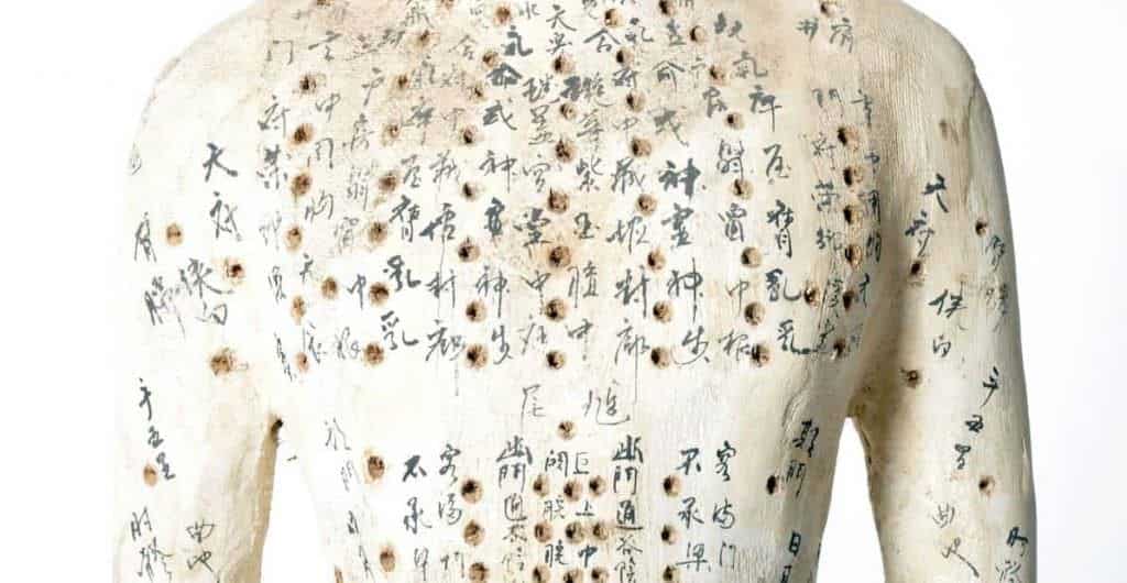 Estatua antiga de tronco humano em laca clara, coberta de caracteres chineses e pequenos pontos marcados sobre o corpo