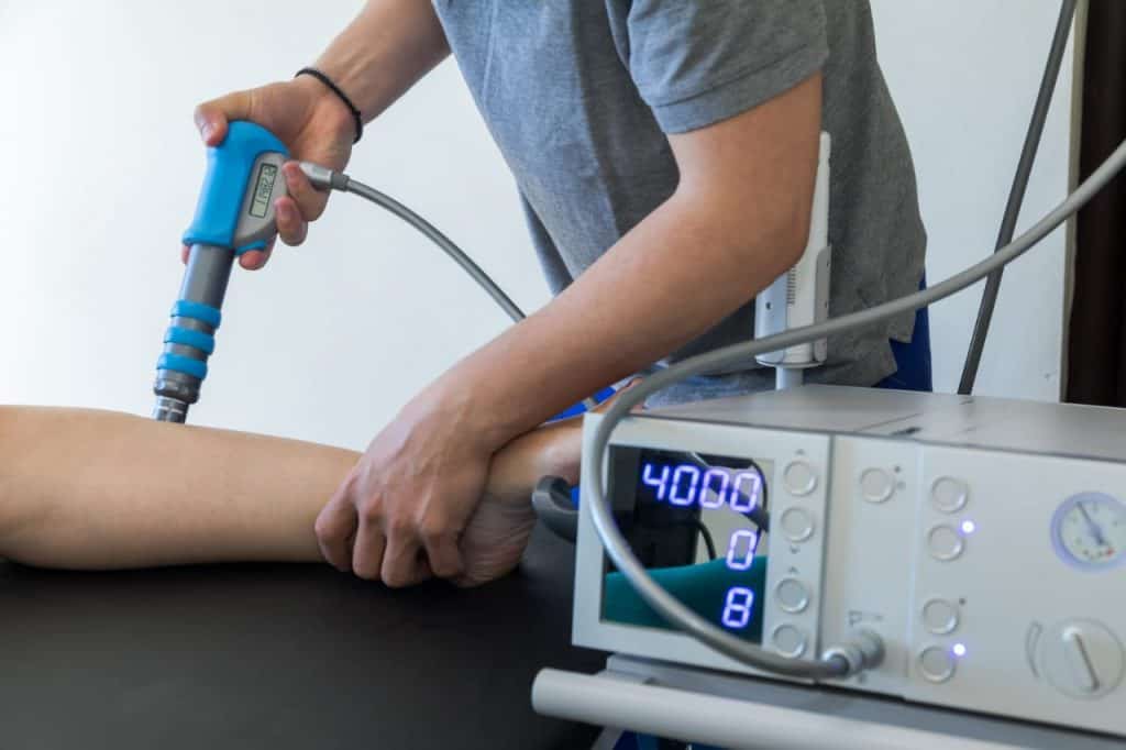 Fisioterapeuta aplicando aparelho de terapia por ondas de choque no antebraço de um paciente, com o painel do equipamento marcando 4000 disparos