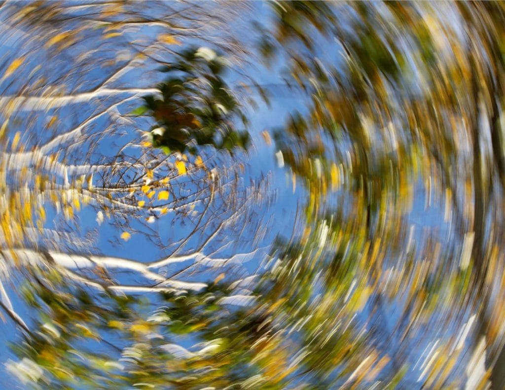 Imagem de árvores e céu registrada em movimento giratório, formando um borrão circular que simula a sensação de rodopio.
