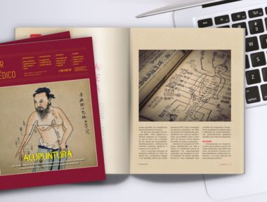 Revista médica aberta sobre um notebook, com uma reportagem sobre acupuntura.
