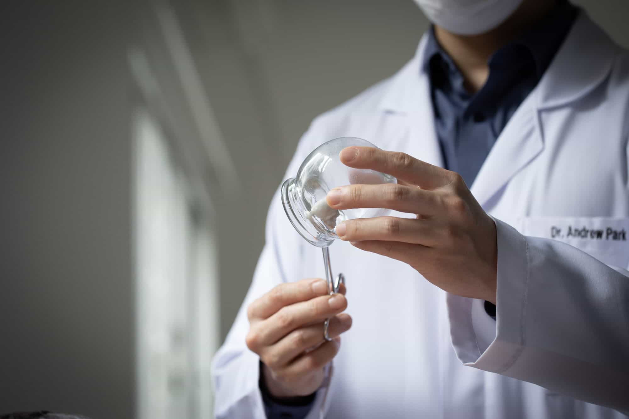 As mãos de Dr. Andrew Park seguram uma ventosa de vidro e uma pinça com algodão.
