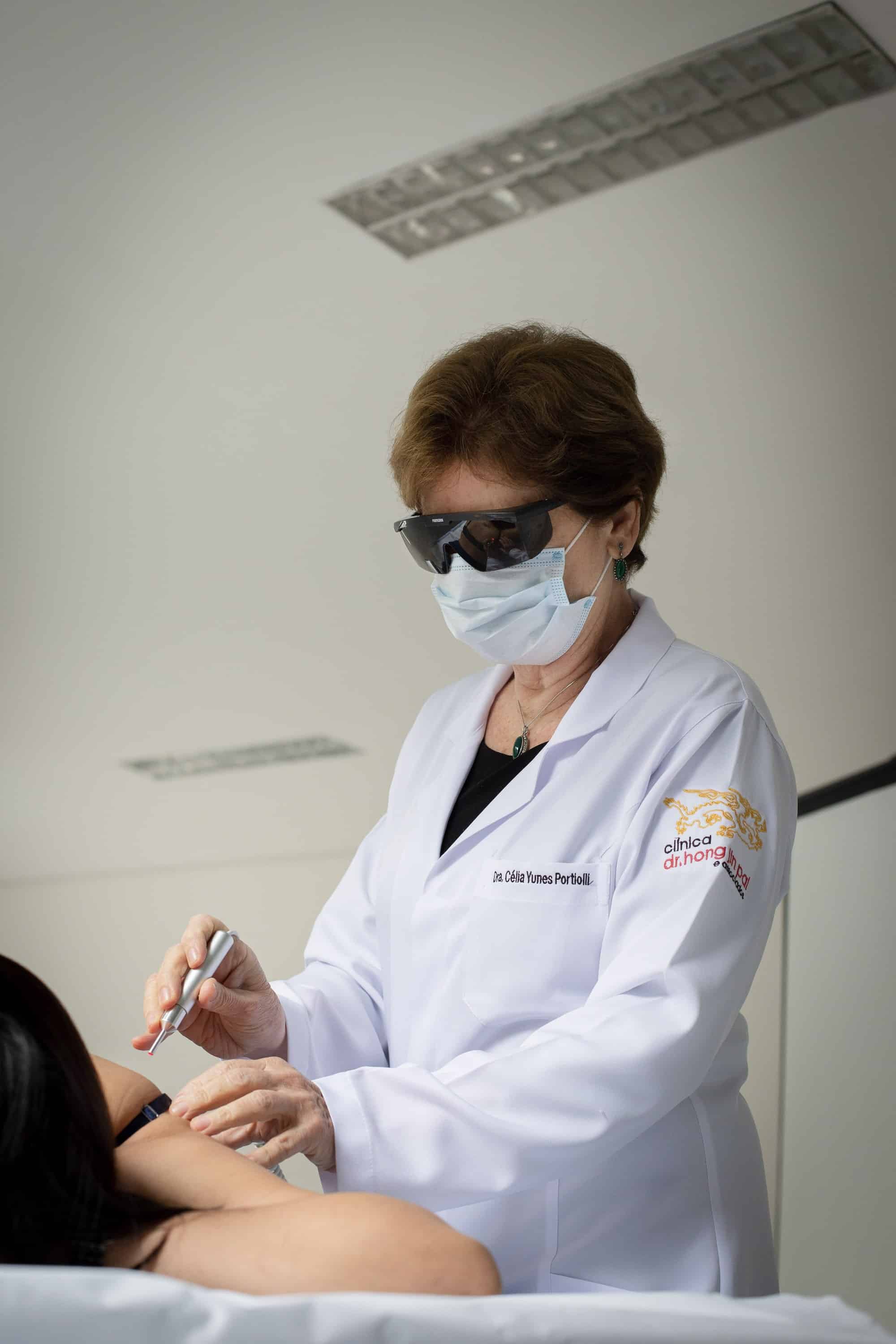 Dra. Célia Yunes Portiolli aplica laser no ombro de uma paciente.