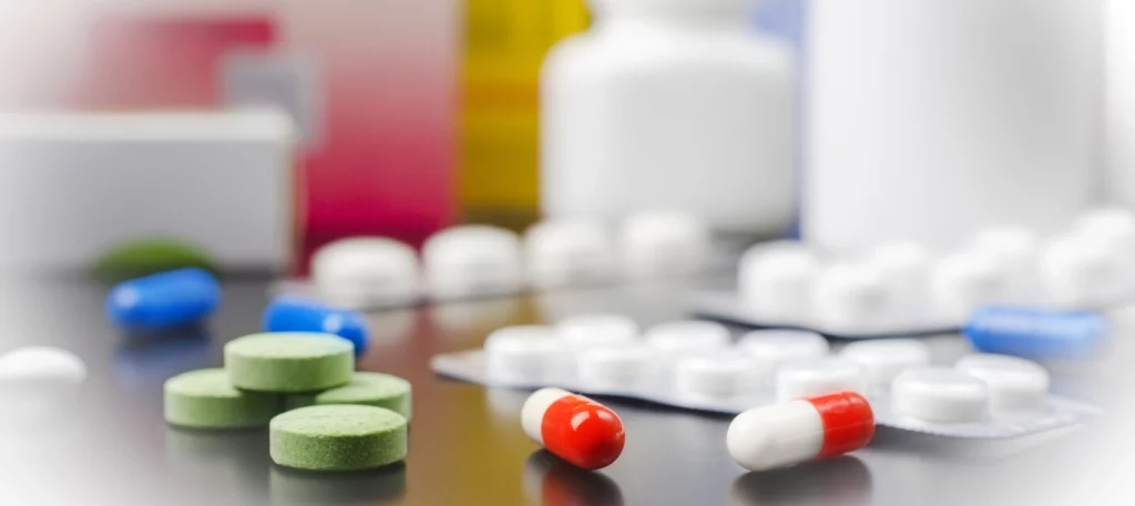 Comprimidos coloridos, cápsulas e cartelas de medicamentos espalhados sobre uma superfície ao lado de frascos