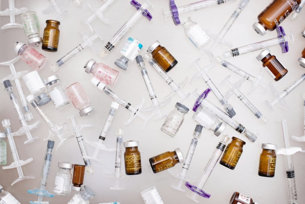 Diversos frascos de medicamento e seringas de aplicação dispostos sobre uma superfície clara.