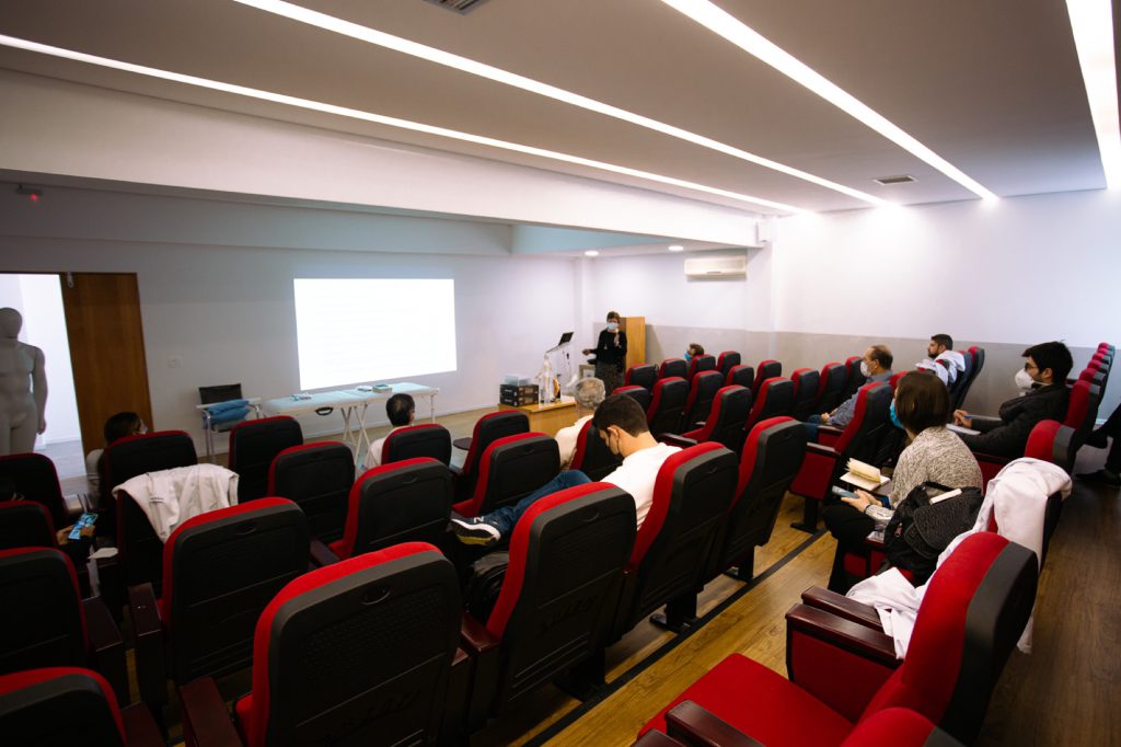 Auditorio com instrutora apresentando aula e maca de demonstração a frente