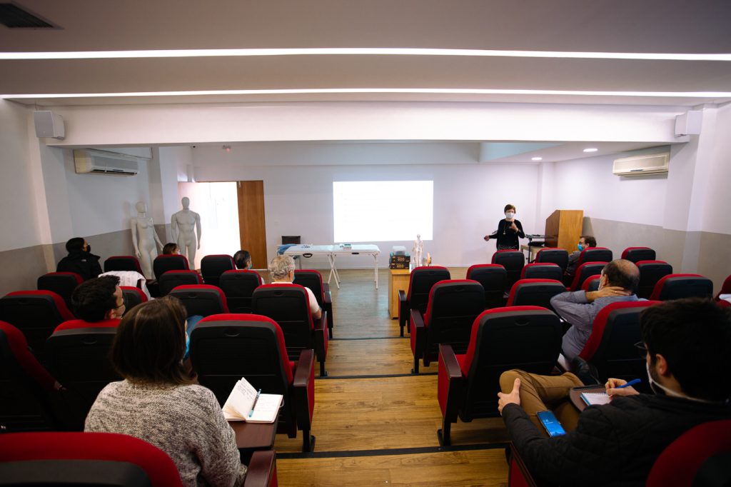 Auditorio amplo com instrutora, manequins anatômicos e alunos durante aula