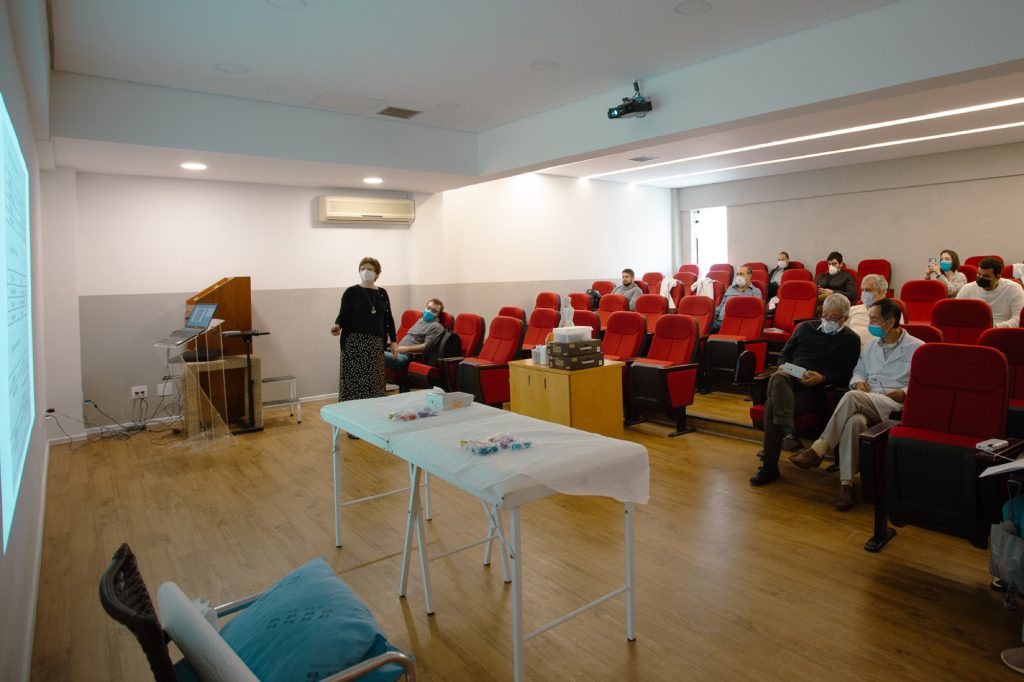 Instrutora apresentando aula no auditorio com mesa de materiais a frente