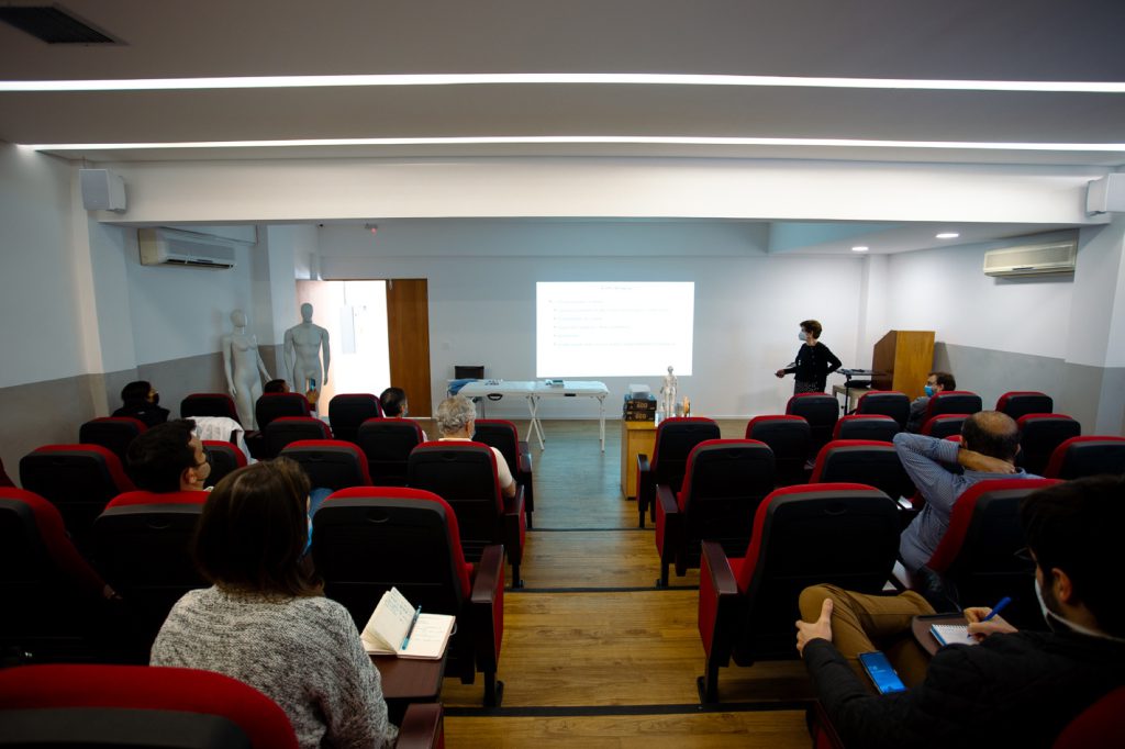 Aula no auditorio do CEIMEC com instrutora e alunos assistindo a apresentação sobre acupuntura
