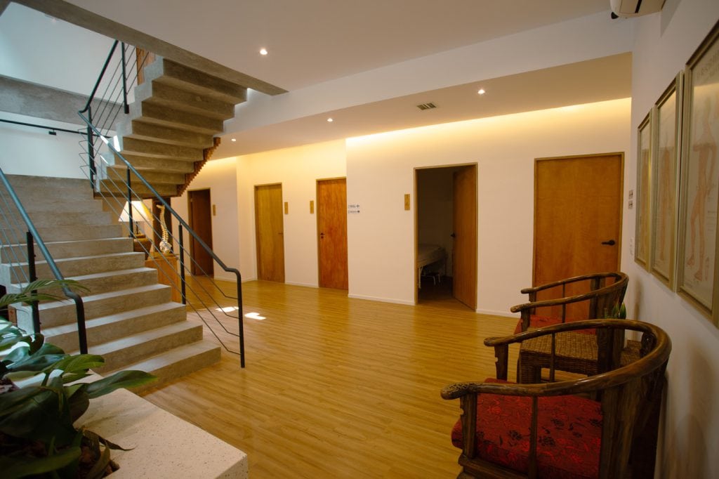 Corredor interno com escada de concreto, piso de madeira e portas das salas de tratamento da clínica