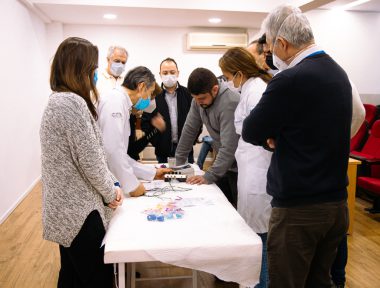 Alunos em pe ao redor da mesa observando demonstracao de eletroacupuntura