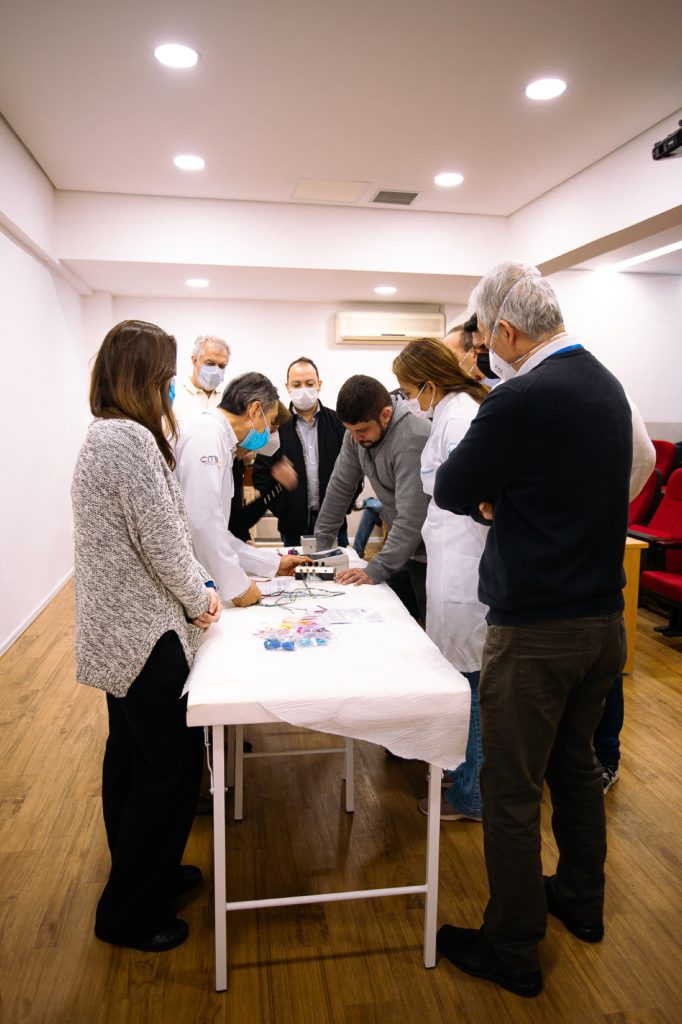 Alunos em pe ao redor da mesa observando demonstracao de eletroacupuntura