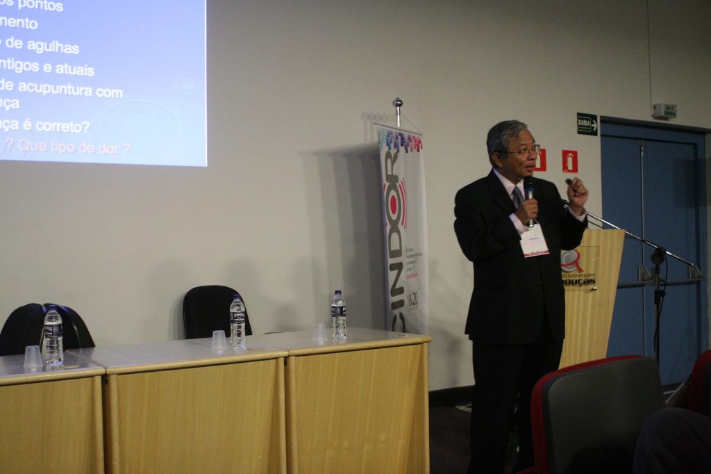 Dr. Hong Jin Pai palestrando ao microfone em congresso sobre dor e acupuntura