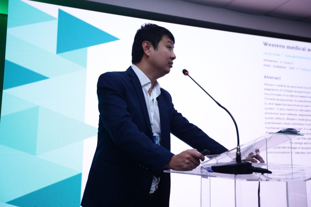 Dr. Marcus Yu Bin Pai discursando no pulpito sobre acupuntura medica ocidental com artigo no telao
