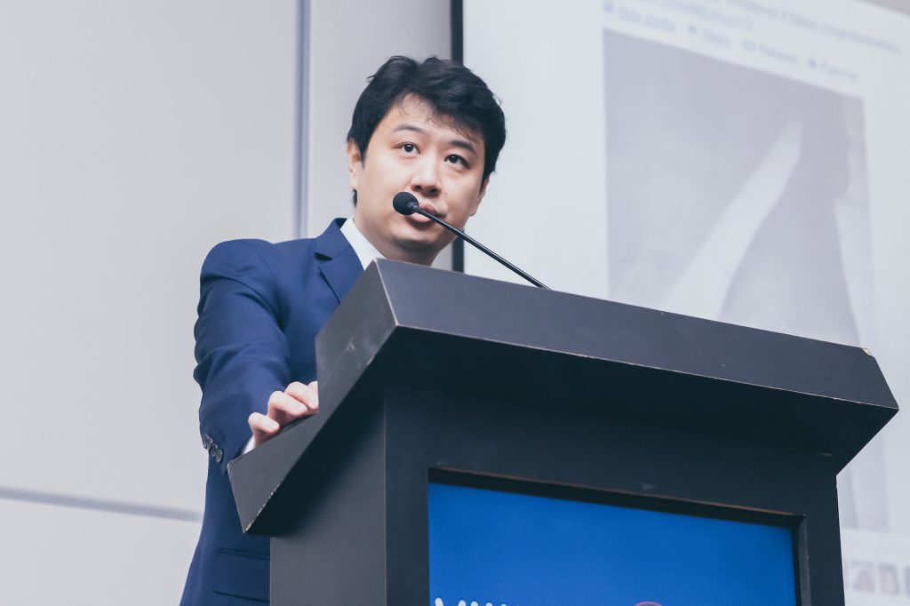 Dr. Marcus Yu Bin Pai palestrando no pulpito com microfone em congresso médico