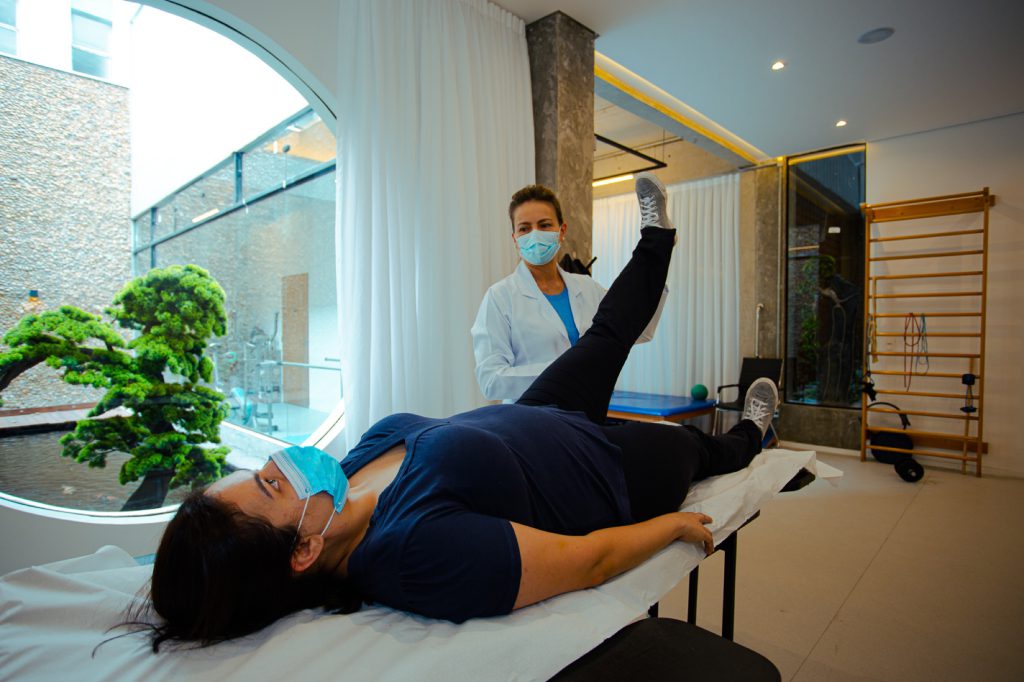 Coxartrose - Artrose no Quadril 2 Fisioterapeuta supervisionando exercício de elevação da perna de paciente deitada na maca