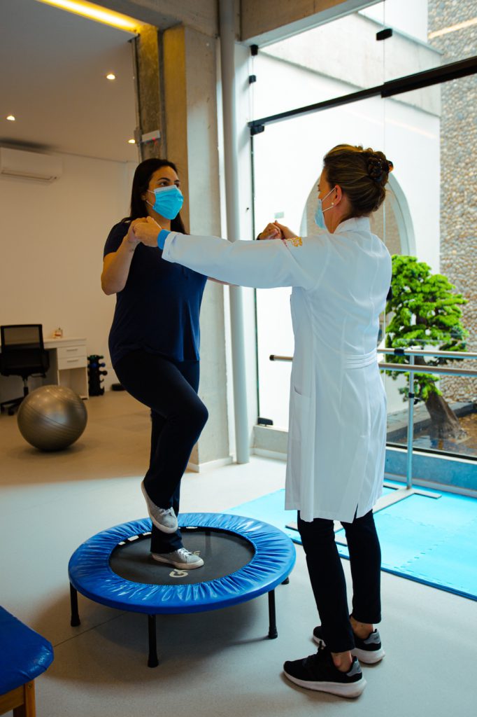 Fisioterapeuta guiando paciente em exercício de equilíbrio sobre minicama elástica