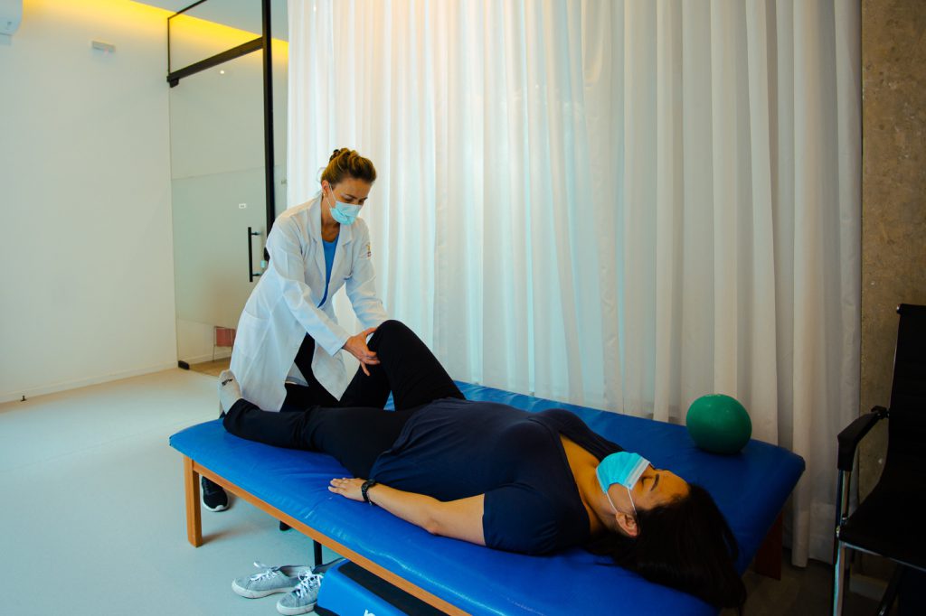 Fisioterapeuta mobilizando o joelho de paciente deitada em colchonete azul de fisioterapia