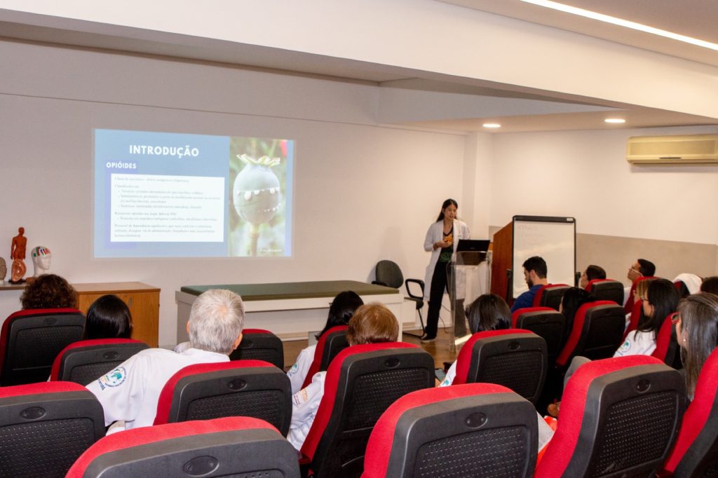 Medica apresentando aula sobre opioides em auditorio para plateia sentada