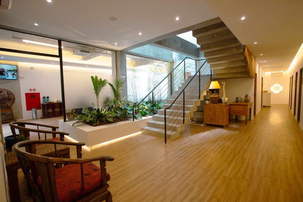 Recepção ampla com jardim interno, escada de concreto e piso de madeira na clínica