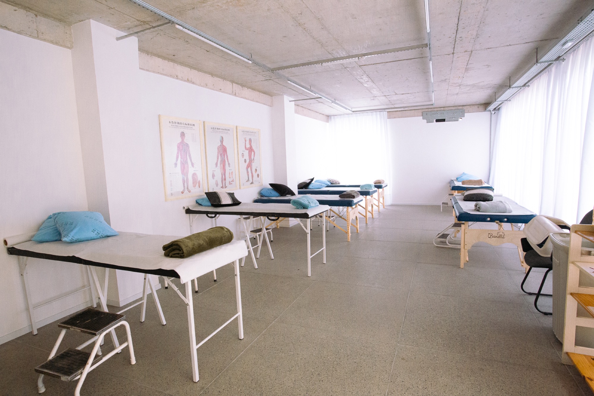 Sala de tratamento da clínica, com macas de acupuntura enfileiradas e pranchas de meridianos na parede
