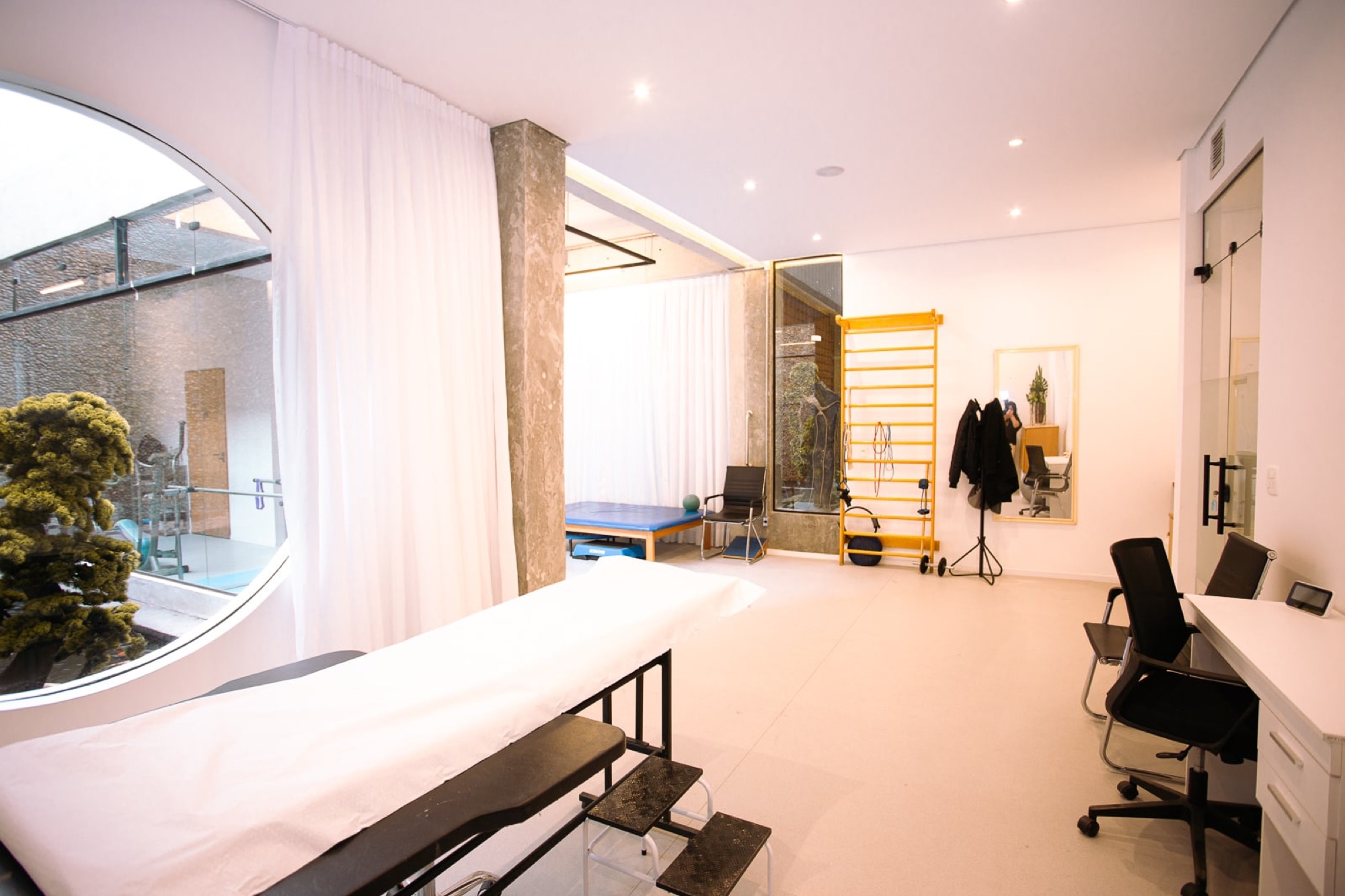 Sala de fisioterapia ampla e iluminada, com maca e espaldar
