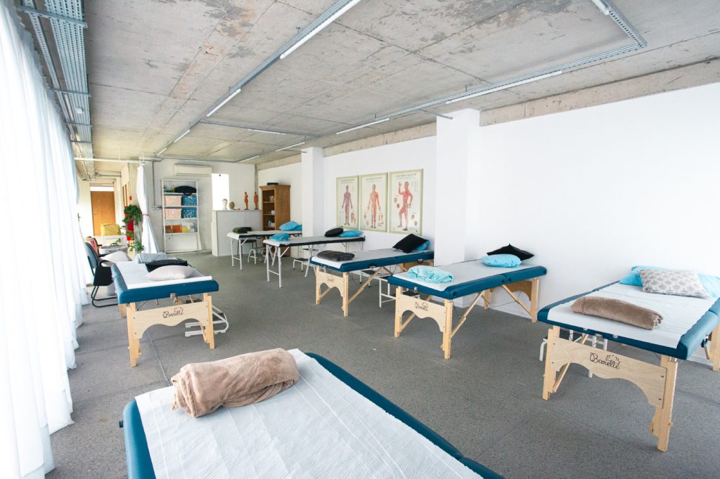 Dor no tornozelo: Principais causas e tratamentos 7 Sala ampla de fisioterapia com várias macas de madeira e teto de concreto aparente na clínica